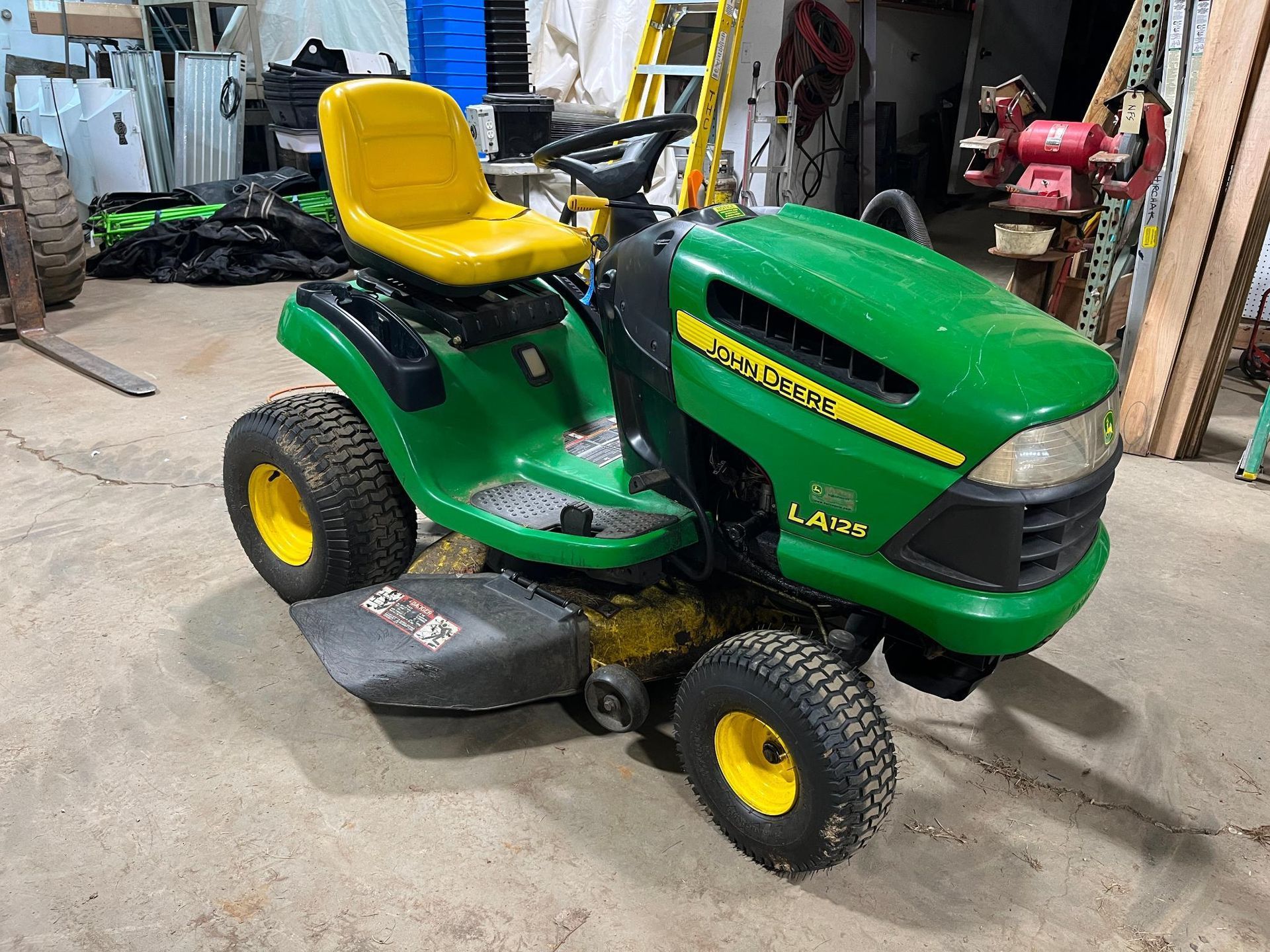 Green John Deere lawn tractor with yellow seat and wheels on a concrete floor.