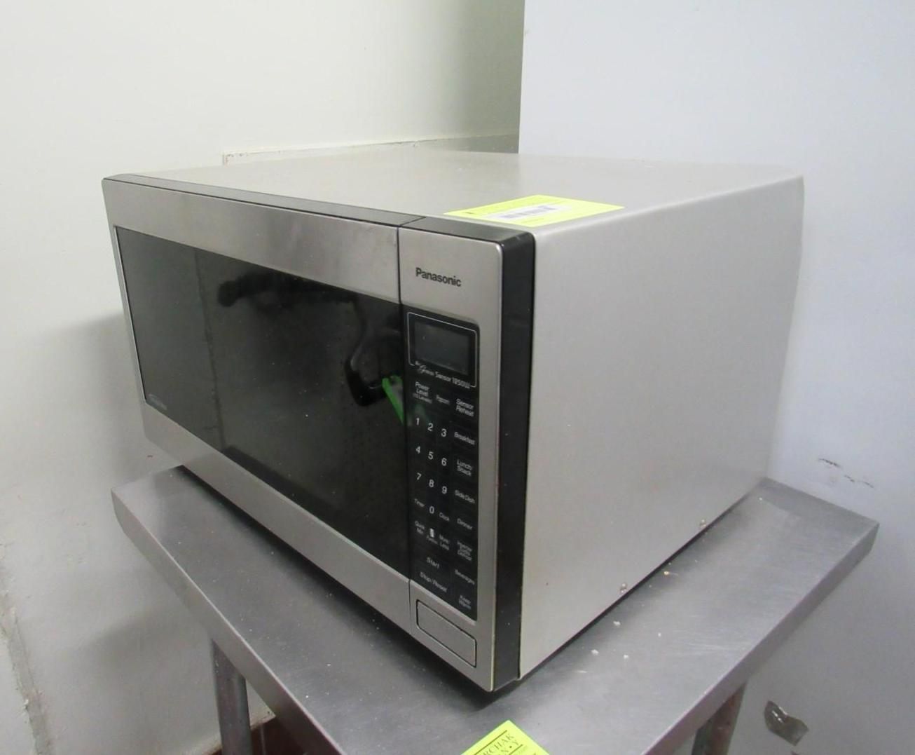 Microwave oven on a stainless steel table, in front of a white wall.