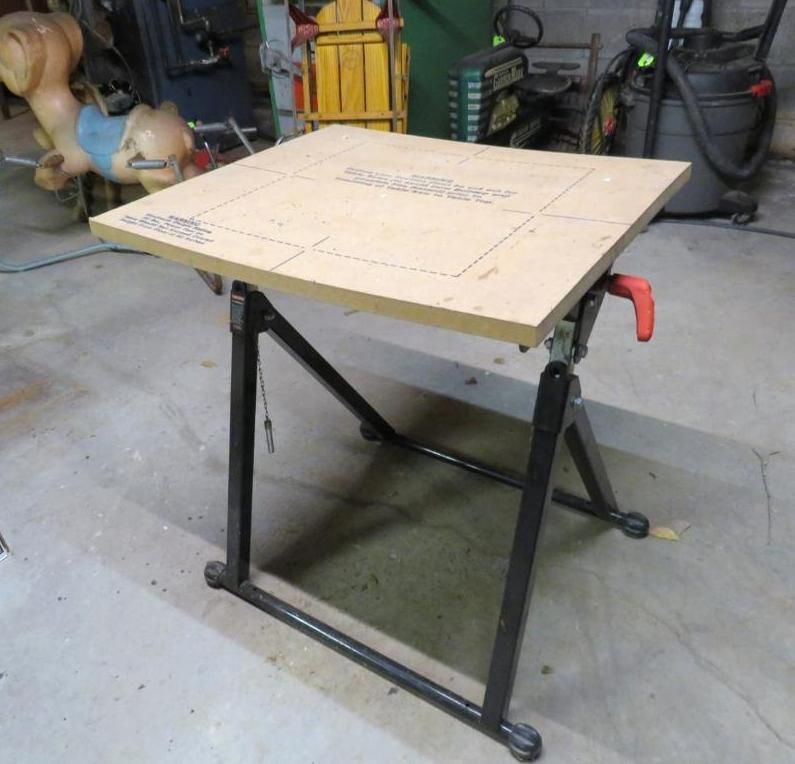 Adjustable height workbench with a light brown tabletop and black metal frame, red lever.