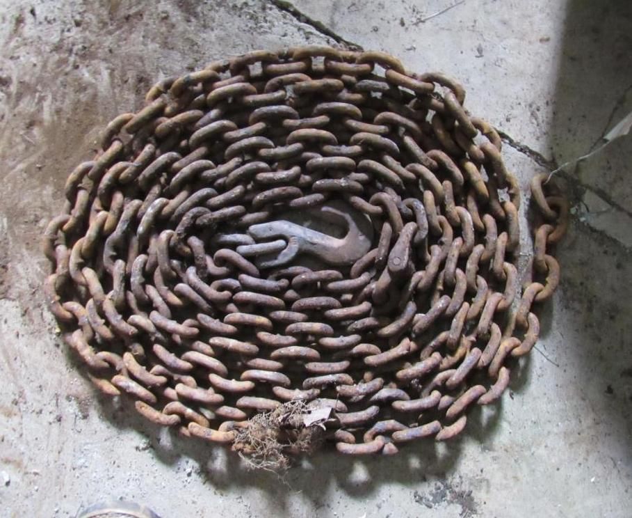 Coiled metal chain with a hook, lying on a light-colored surface.