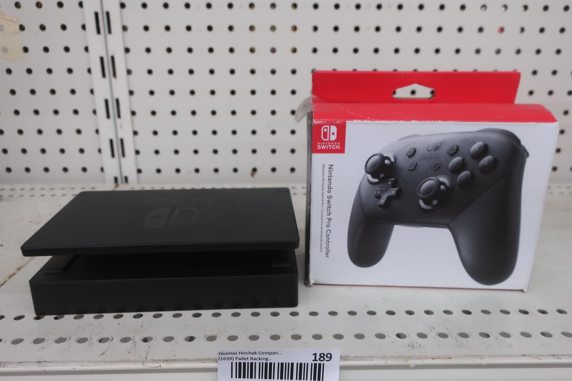 Nintendo Switch dock and Pro Controller box on a shelf. Black dock, controller in box.