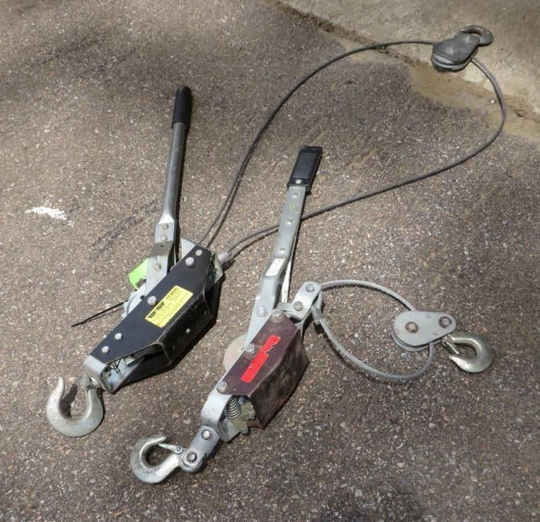 Two cable pullers with hooks and cable, on a concrete surface.