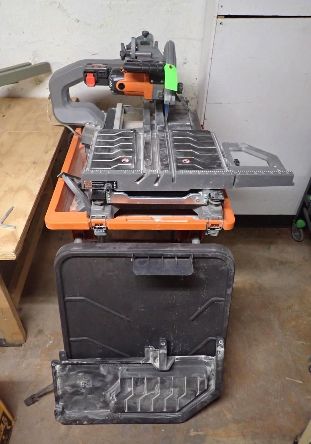 Orange and gray tile saw with black base and water tray in a workshop.