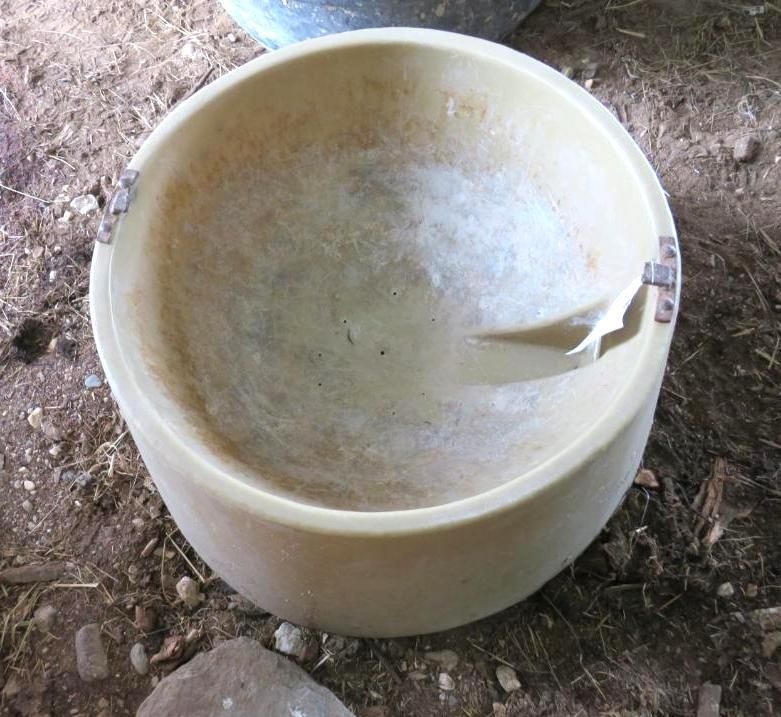 Tan, circular, animal water trough with metal brackets.
