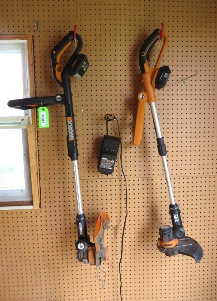 Two Worx electric string trimmers hang on a pegboard wall with a charger.