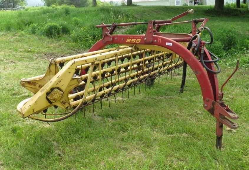Red and yellow hay rake on green grass.