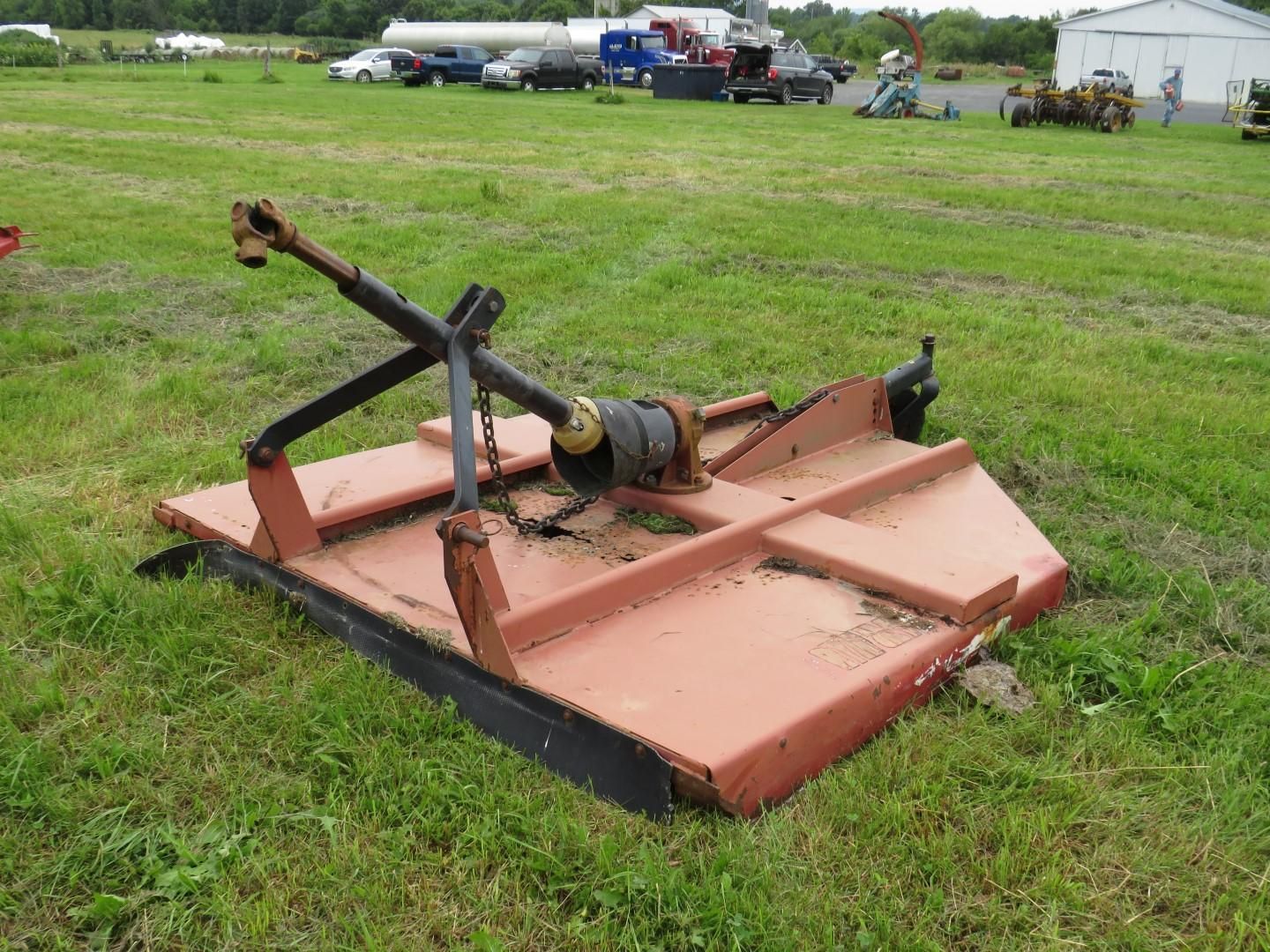 A red, rectangular rotary mower sits in a grassy field.