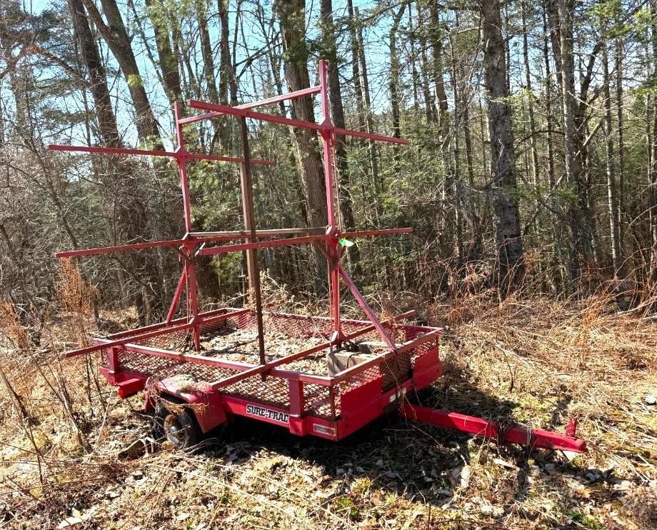 Red utility trailer with a metal frame in a wooded area.