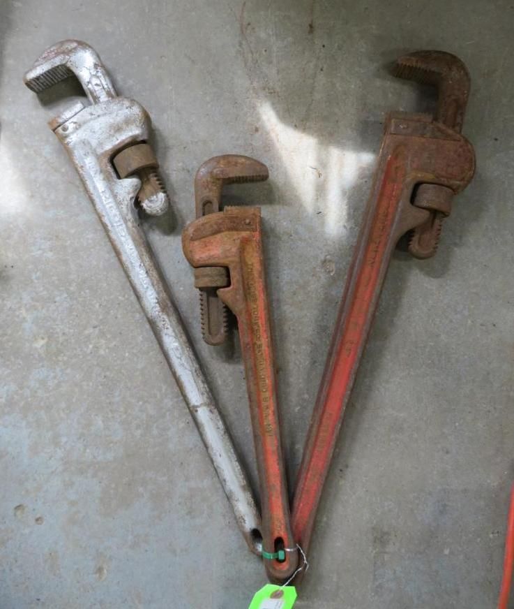 Three pipe wrenches: gray, and red, leaning against a surface.