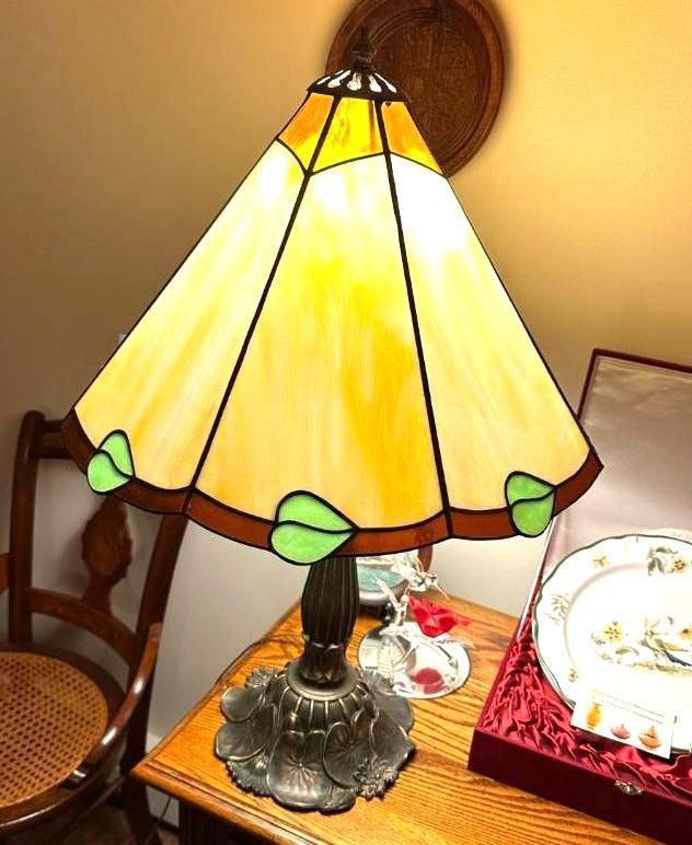 Tiffany-style table lamp with yellow and green stained glass shade, set on a wooden table.