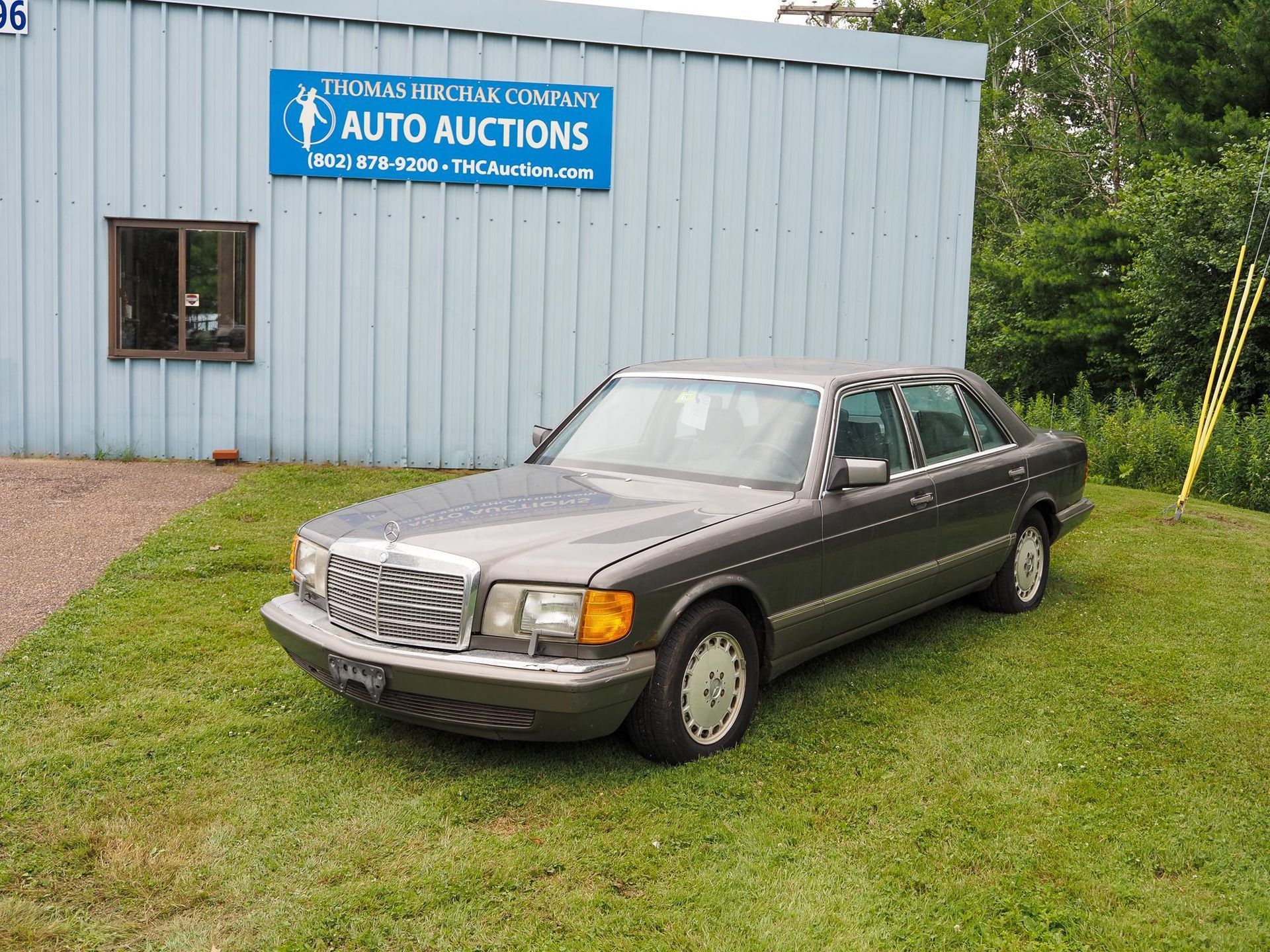 Gray Mercedes sedan parked on grass in front of an auto auction building.