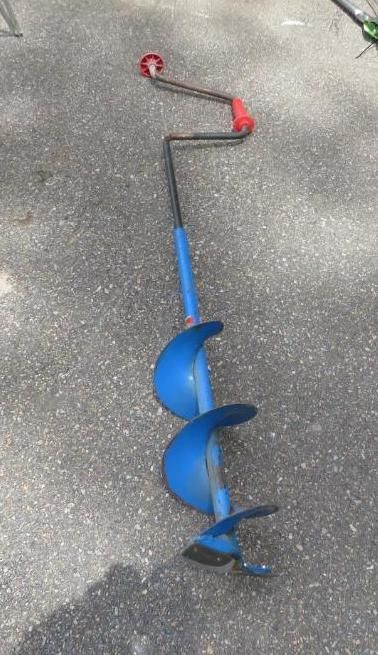 Blue and black ice auger with a red handle lying on gray concrete.