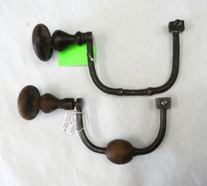 Two antique hand drills with wooden handles and metal frames on a white surface.