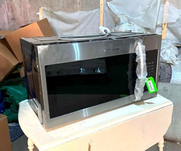 Stainless steel microwave on a small white table, with a green tag.