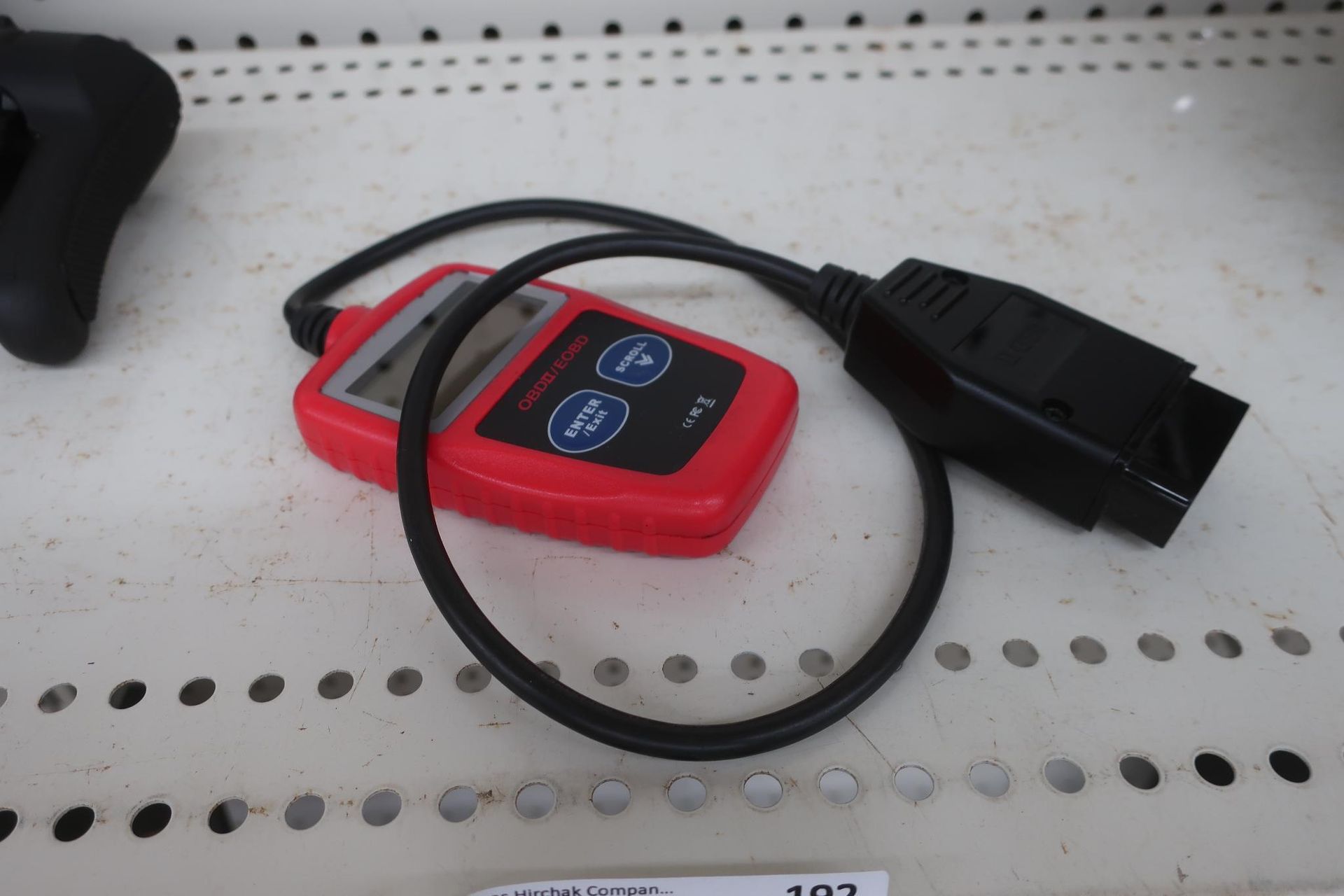 Red and black OBD2 code reader on a white surface with perforated holes.