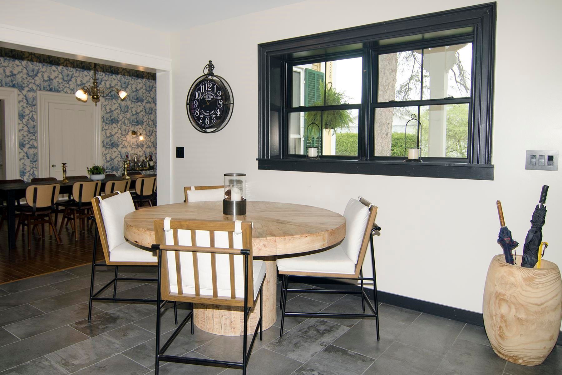 A dining area with a round table, chairs, and a window with a black frame.