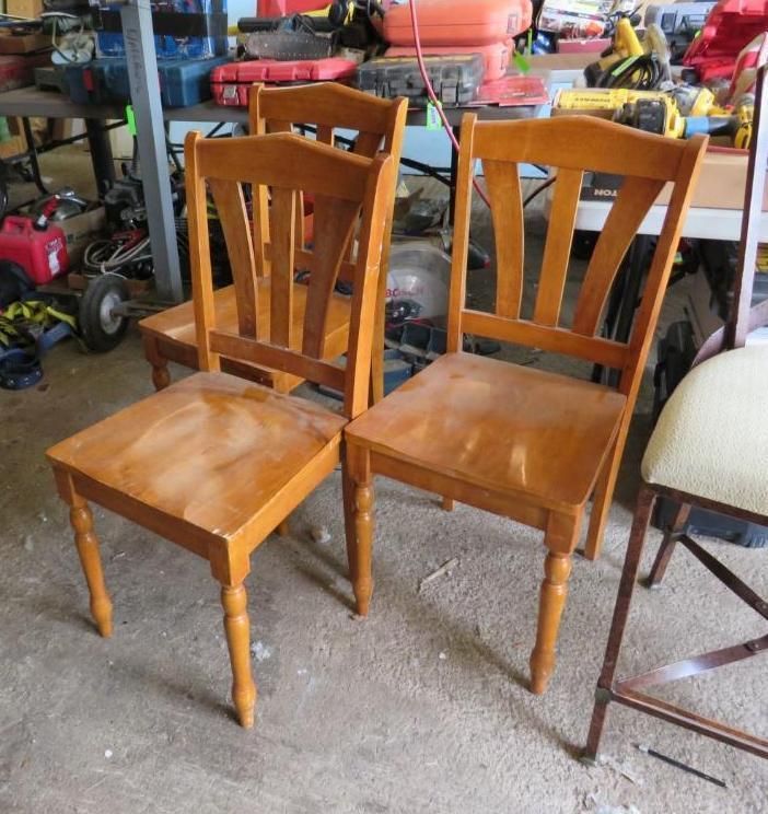 Four wooden chairs in a garage, two visible with slightly curved backs and light brown finish.