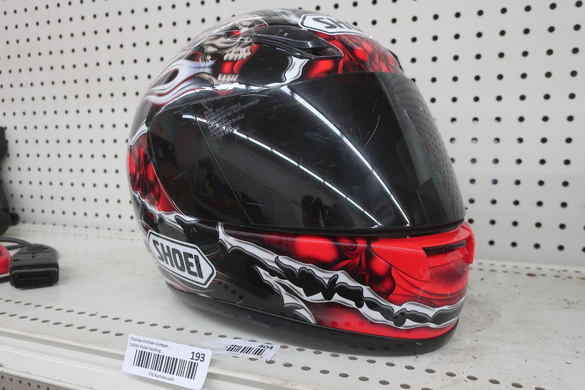Black and red Shoei motorcycle helmet on a shelf, with a dark visor and graphic design.