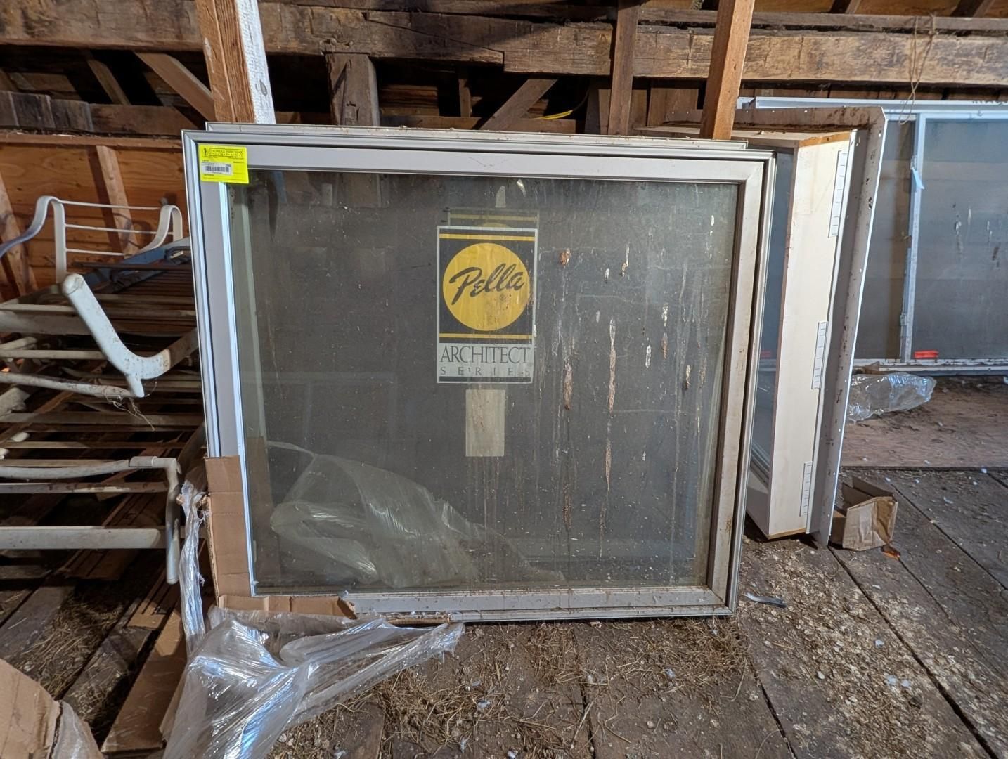 Wrapped window frame leaning against a wooden wall in a rustic interior, with a yellow sticker on the glass.