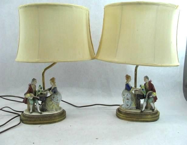 Two porcelain lamps with cream shades. Figurines of people seated at a table on the bases.