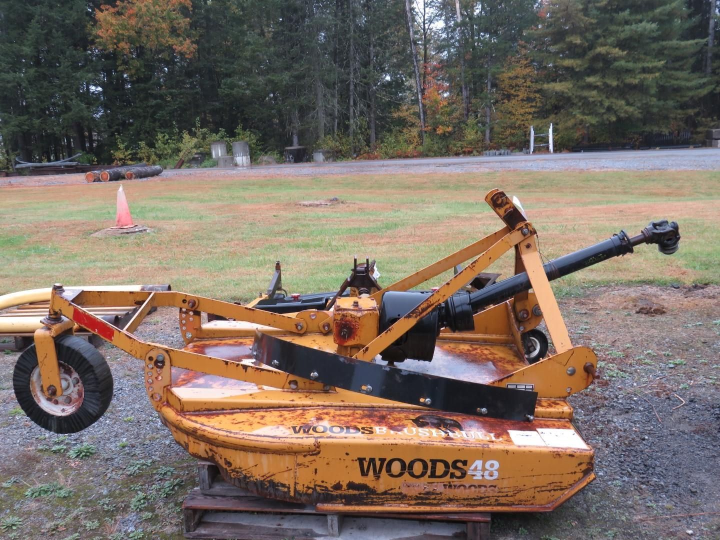 Yellow Woods 48 rotary mower on a pallet in a grassy field with trees in the background.