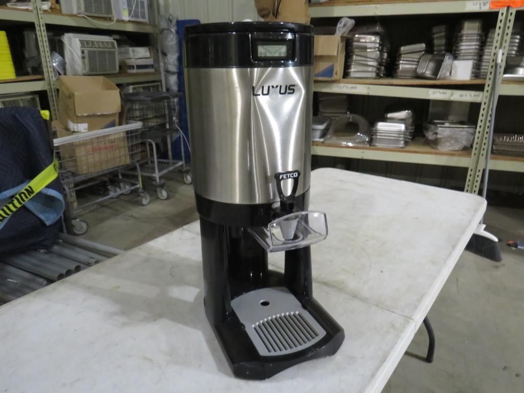 Stainless steel coffee urn on a table in a storage room.