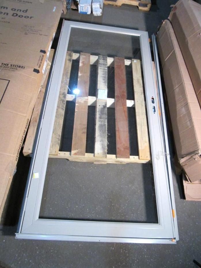 White framed glass door lying on a wooden pallet; cardboard boxes in the background.