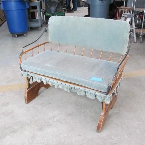 Antique wooden bench with blue upholstered seat and back, metal accents, and a ruffled skirt.