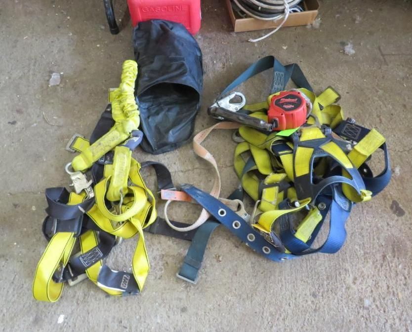 Safety harnesses and equipment on the ground: yellow and blue harnesses, bag, and tape measure.