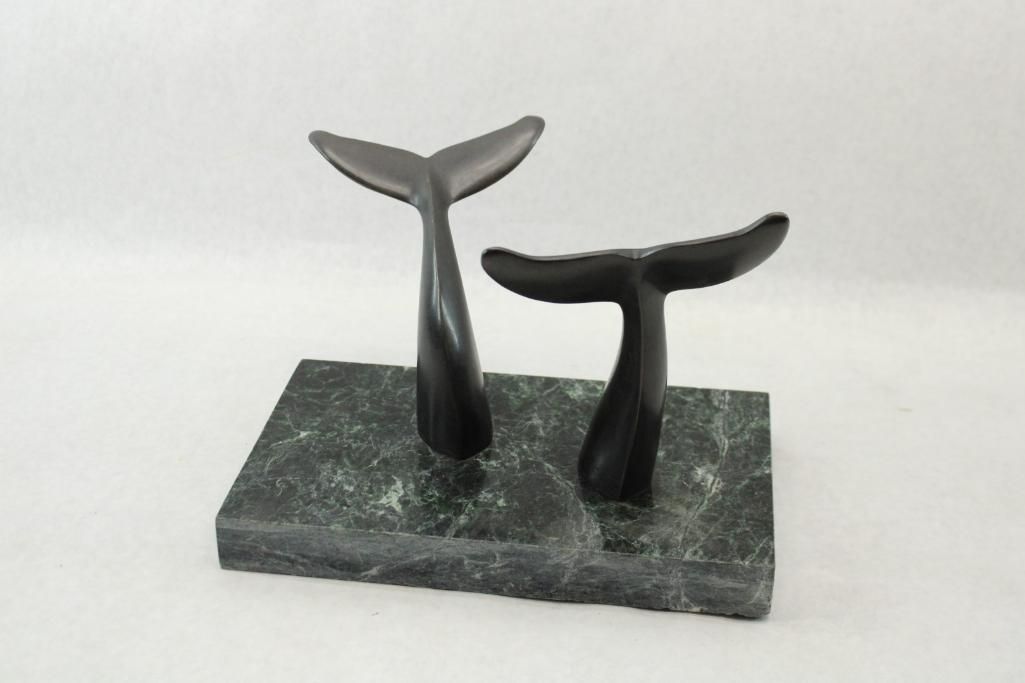 Two bronze whale tail sculptures on a green marble base.