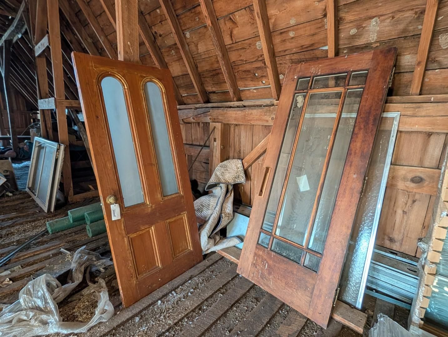 Two wooden doors leaning in an attic with exposed rafters and stored materials