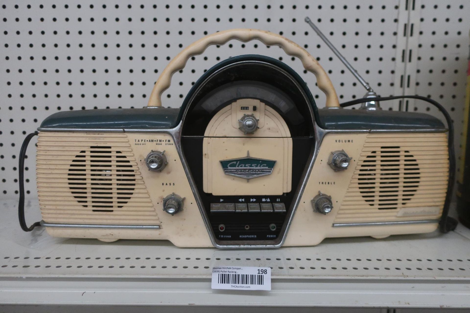 Cream and teal retro radio with handle, knobs, speakers, and antenna on a shelf.