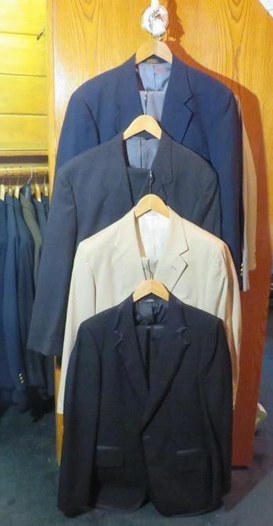 Four suits hanging on a wooden rack: navy, charcoal, beige, and black.