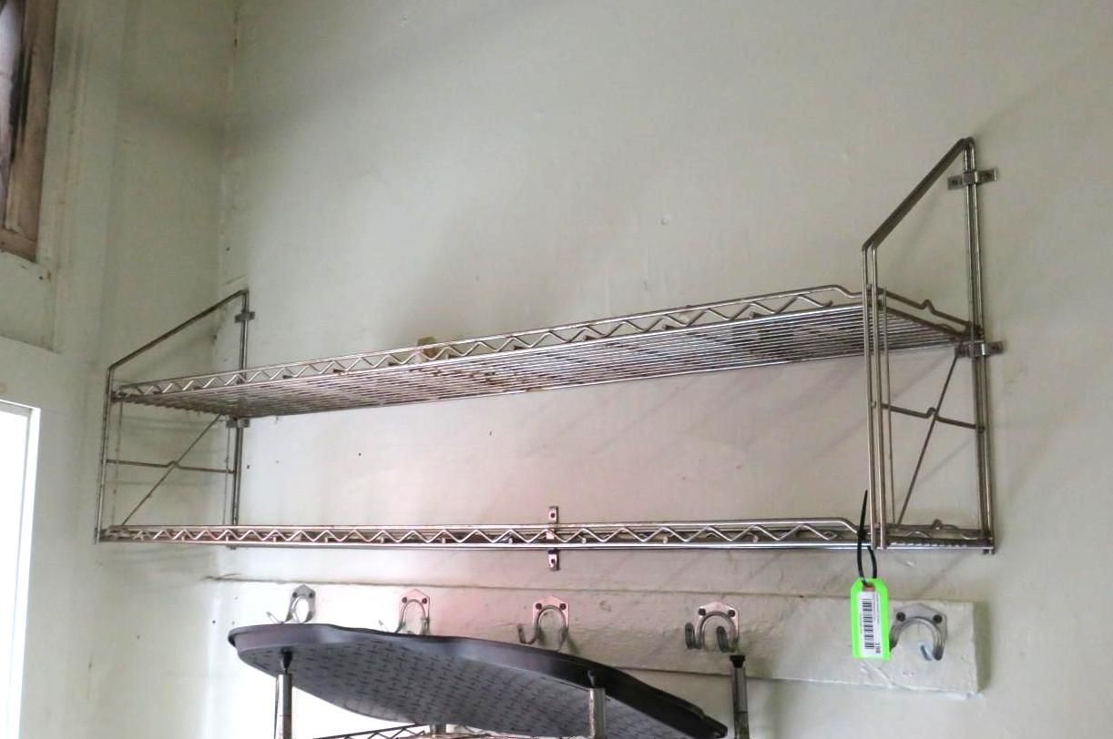 Two-tier metal wire shelf attached to a white wall, with items on the bottom shelf and hooks below.