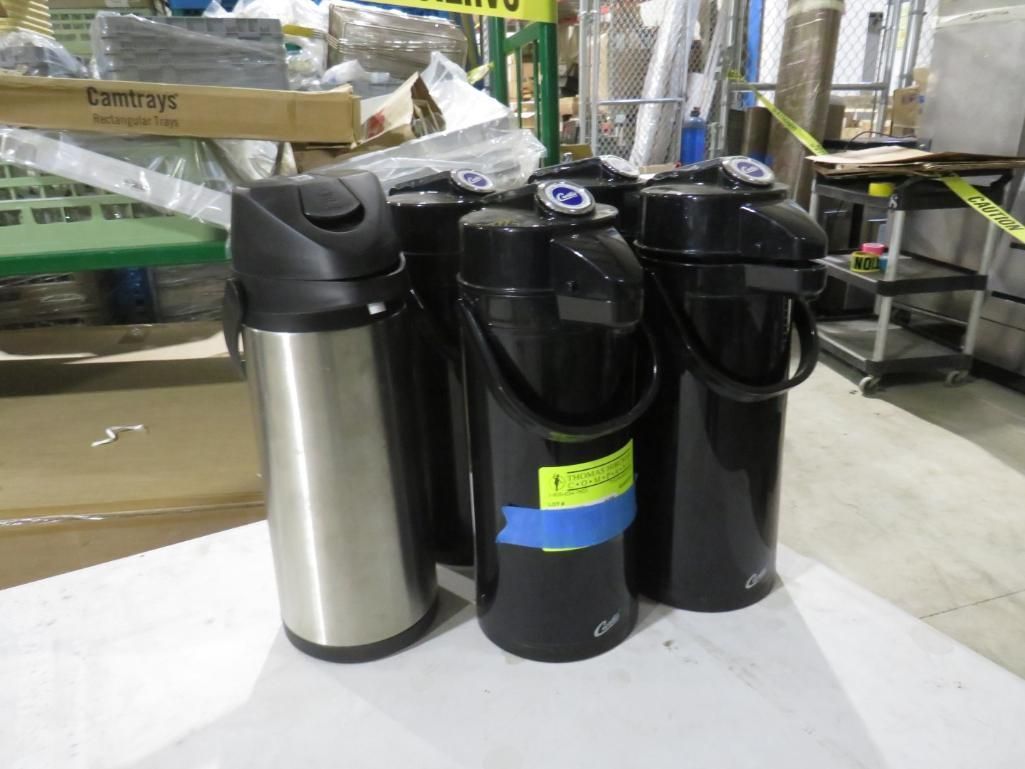 Four beverage dispensers, black and silver, in an industrial setting.