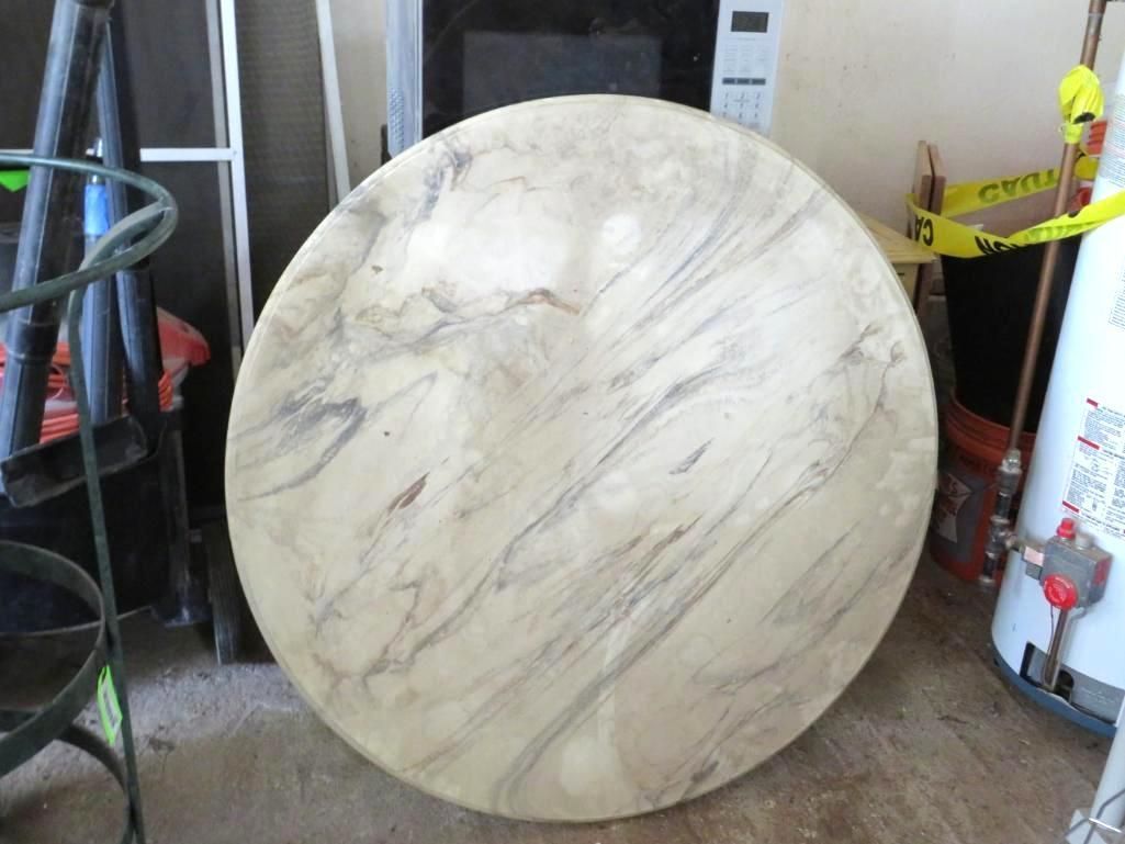Large, round table with a marble-like pattern. Set outdoors, possibly in a garage.