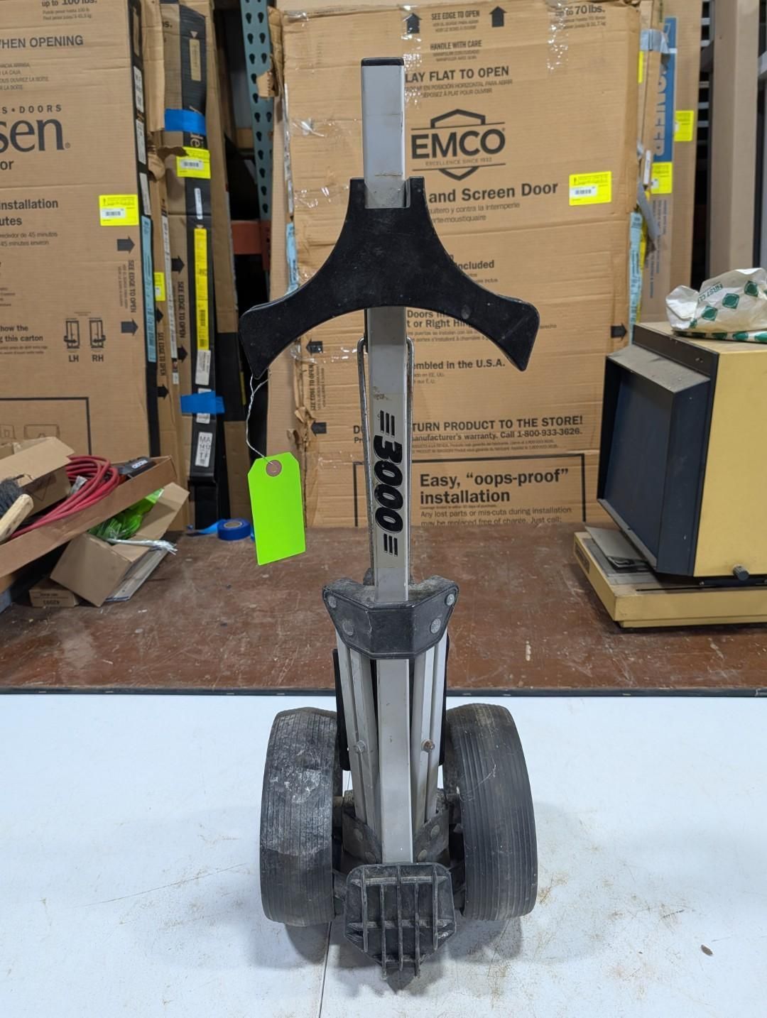 Black floor jack with worn wheels in a warehouse aisle, surrounded by cardboard boxes and tools.