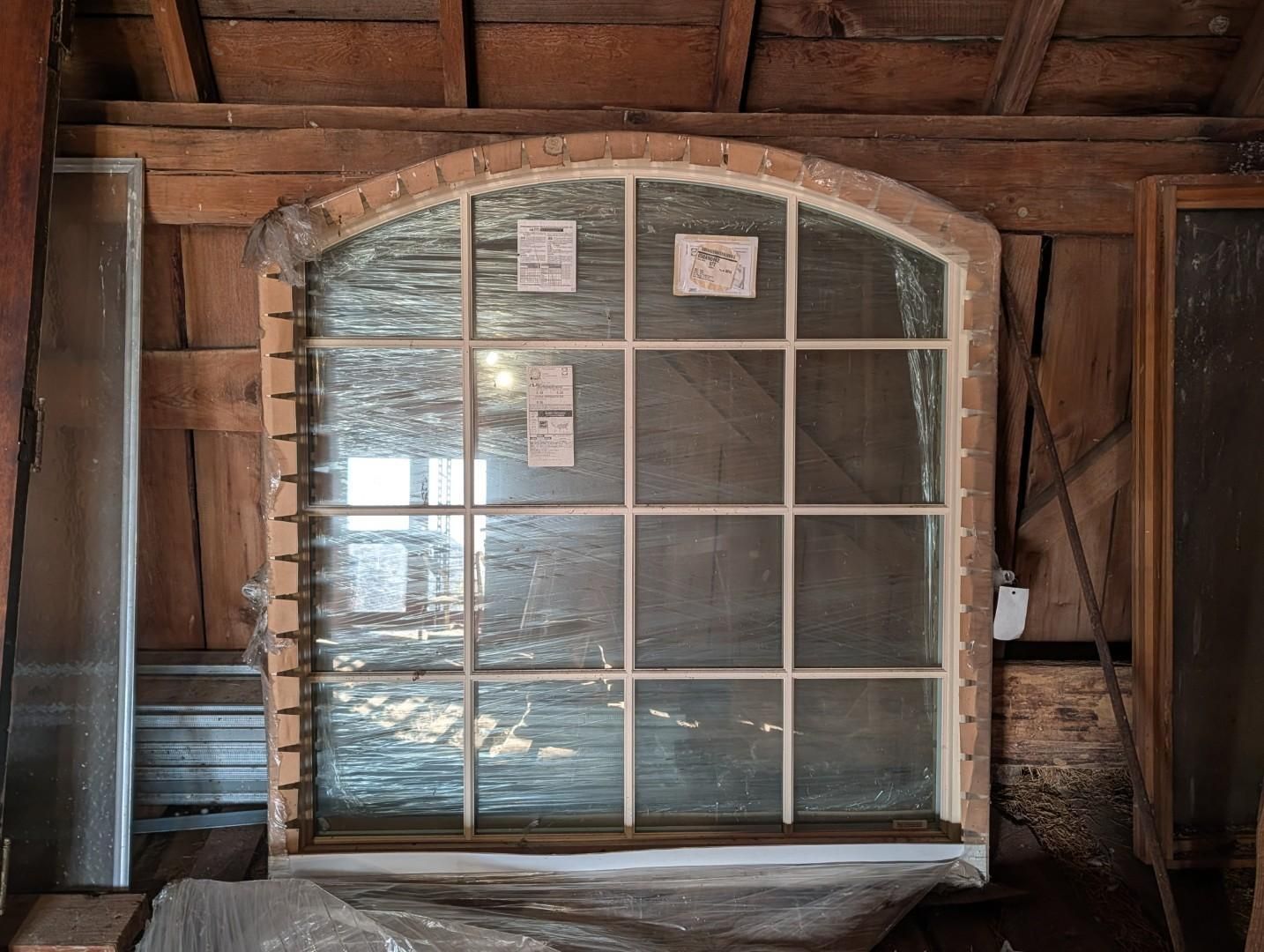 Arched window with multiple panes and plastic sheeting in an unfinished attic wall