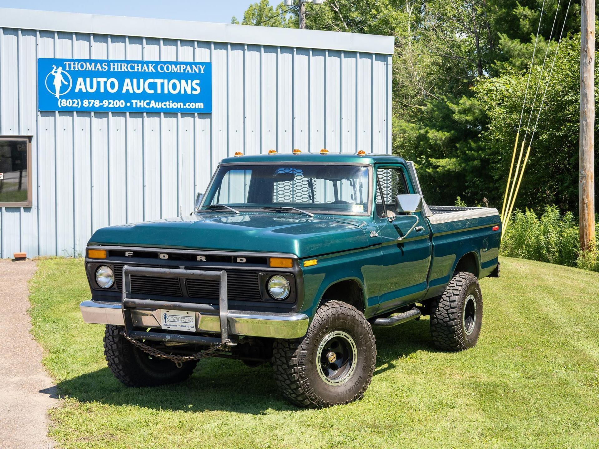 Green Ford pickup truck parked in front of an auto auction building on a sunny day.