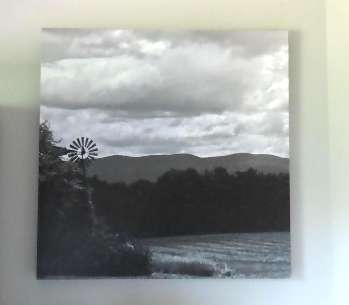 Black and white landscape art with a windmill, mountains, and water under a cloudy sky.