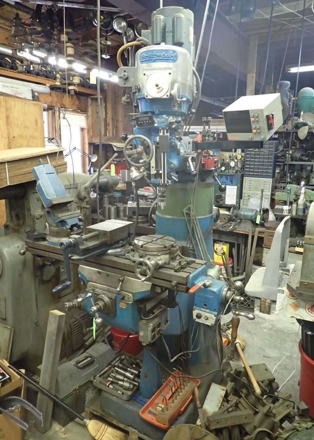 Vertical milling machine in a workshop. Blue and gray, with various tools and equipment.