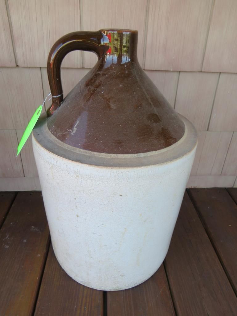 Brown and white stoneware jug with a handle, sitting on a wooden surface.