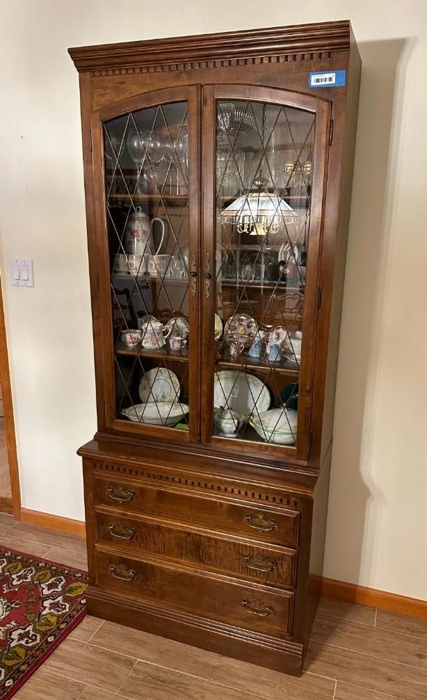 Wooden curio cabinet with glass doors, displaying china and decor.