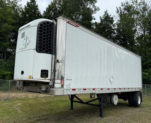 Refrigerated semi-trailer in a grassy field, white with a black cooling unit.