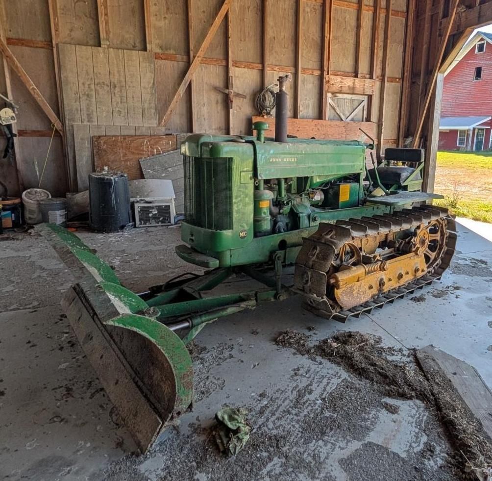 green tractor with a front blade parked inside a rustic barn.