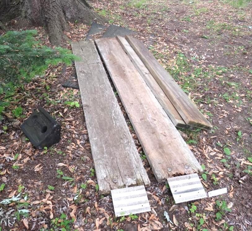 Three wooden planks and a small black block rest on the ground near a tree.