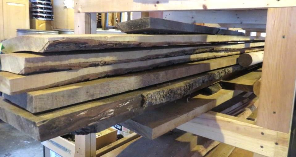 Stack of rough-hewn wooden planks on a rack in a workshop, showcasing natural edges and varying colors.