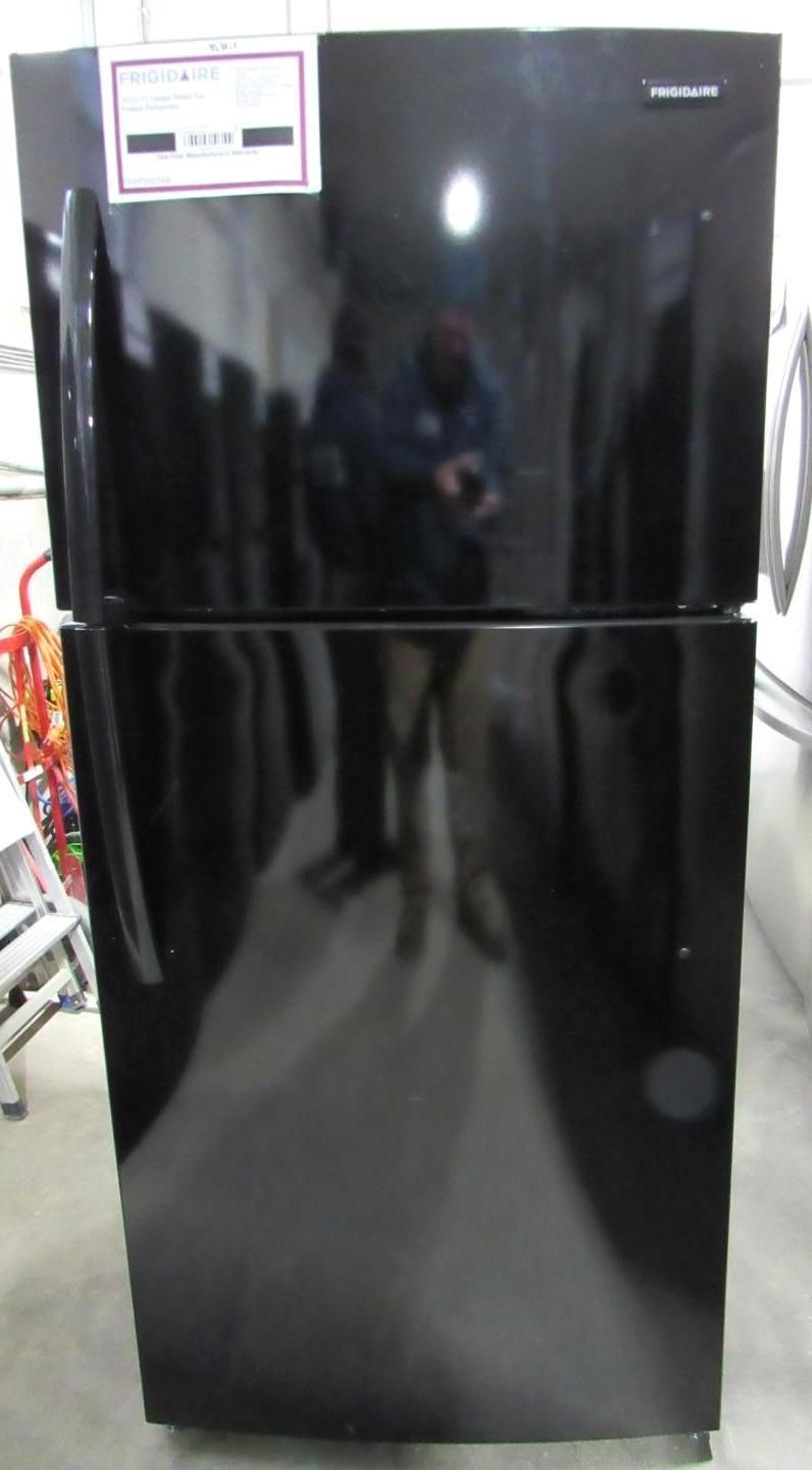 Black refrigerator with top freezer, reflecting a person.