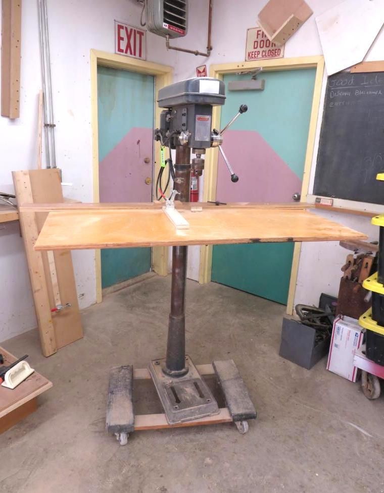 A drill press with a large wooden table in a workshop.