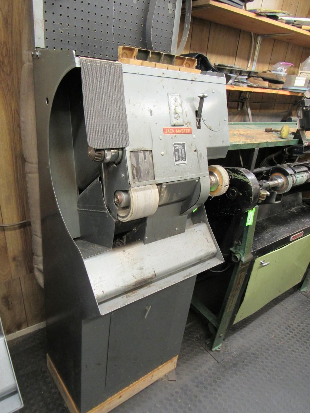 A gray industrial shoe finishing machine with abrasive attachments and a cabinet base, in a workshop setting.